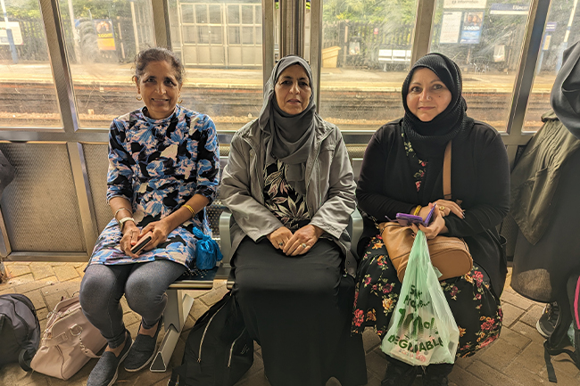 Three women sitting at a bus stop.