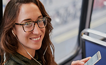 Young woman sat on bus with headphones in and smartphone