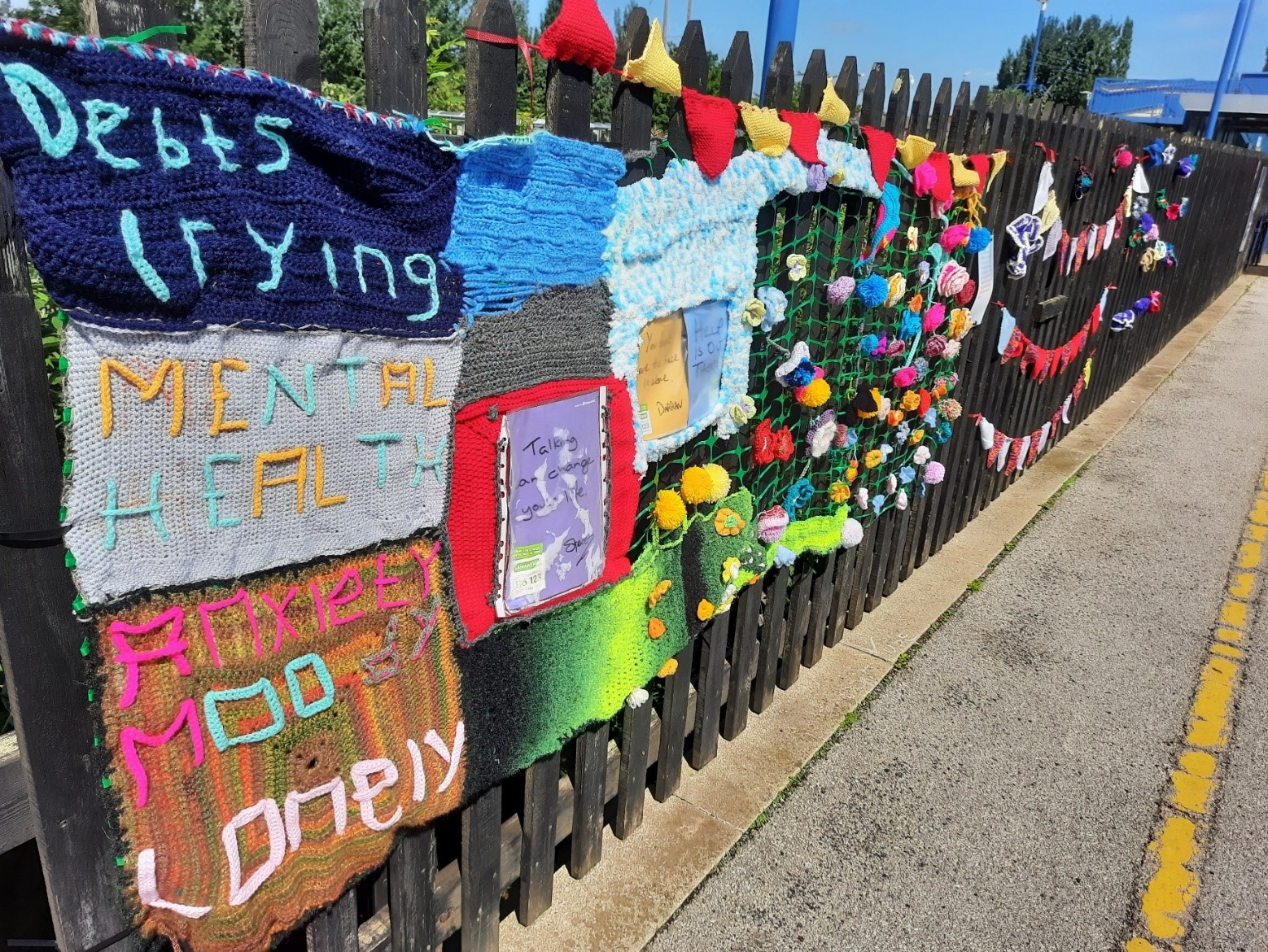 Knitted flowers, rainbows and bunting on a fence